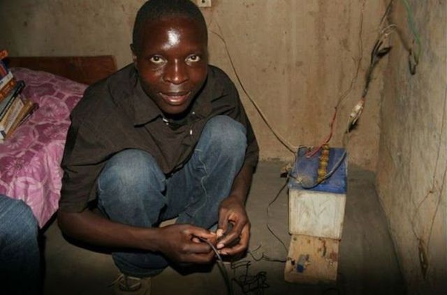 William Kamkwamba squatting in front of a hand-crafted machine