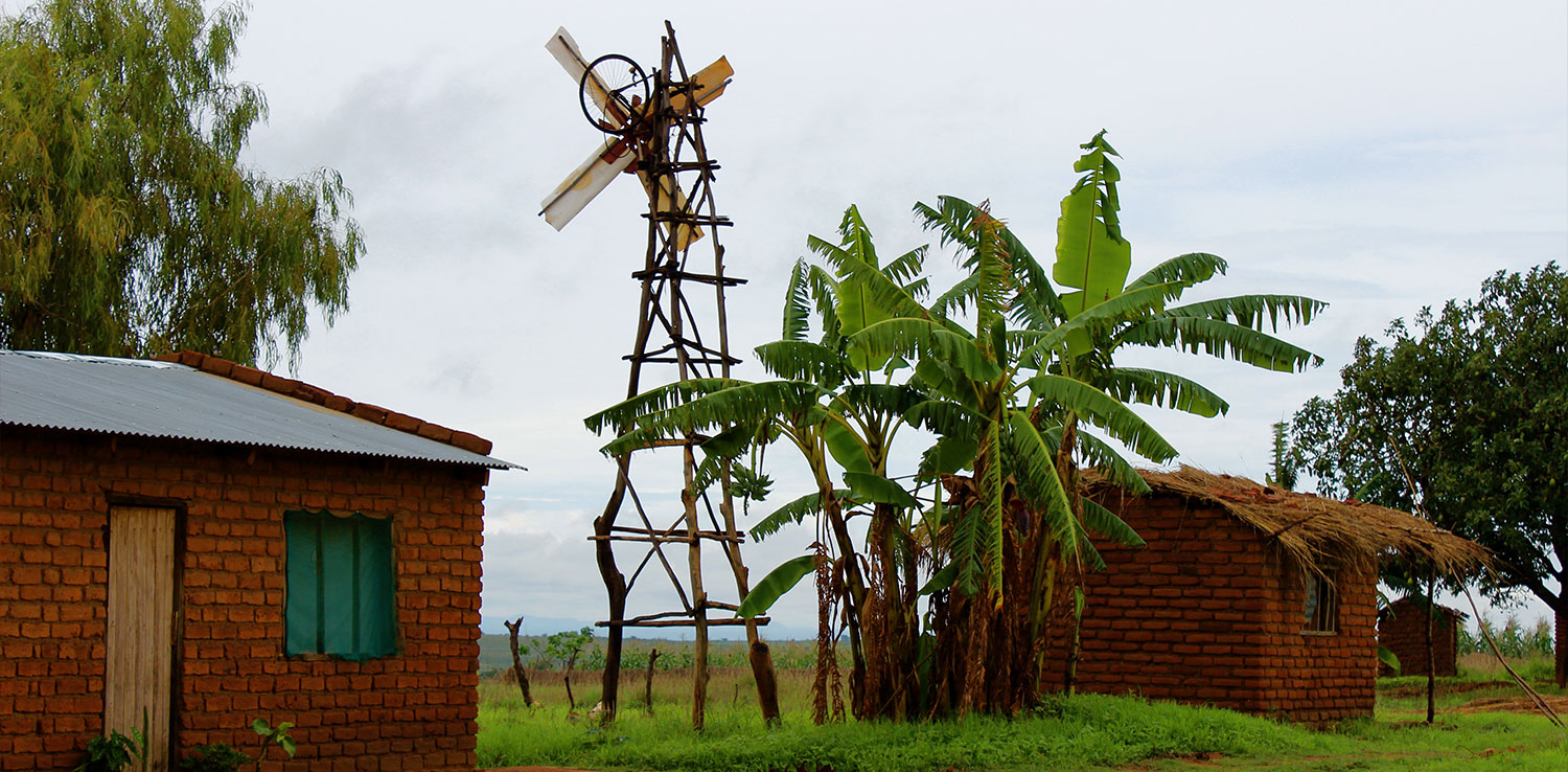 A windmill made of wood between two houses with banana trees