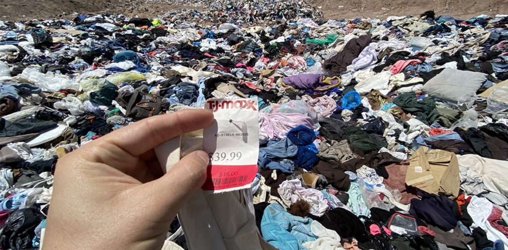 a heap of discarded clothing on a desert with a price tag attached to an unused item in the foreground