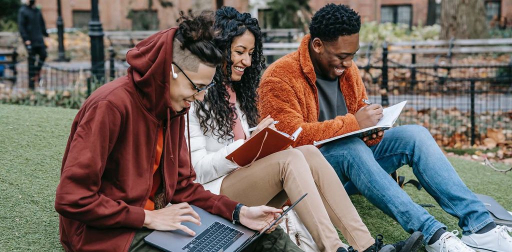 three young adult students sitting at a park and studying happily reflecting sustainability in education