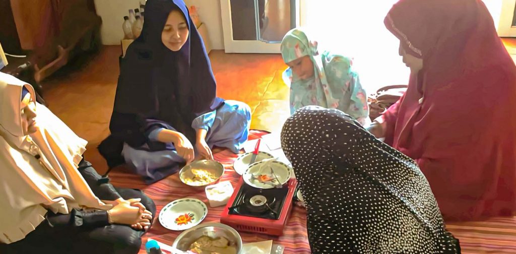 four hijabi women and one child around a stove and several bowls