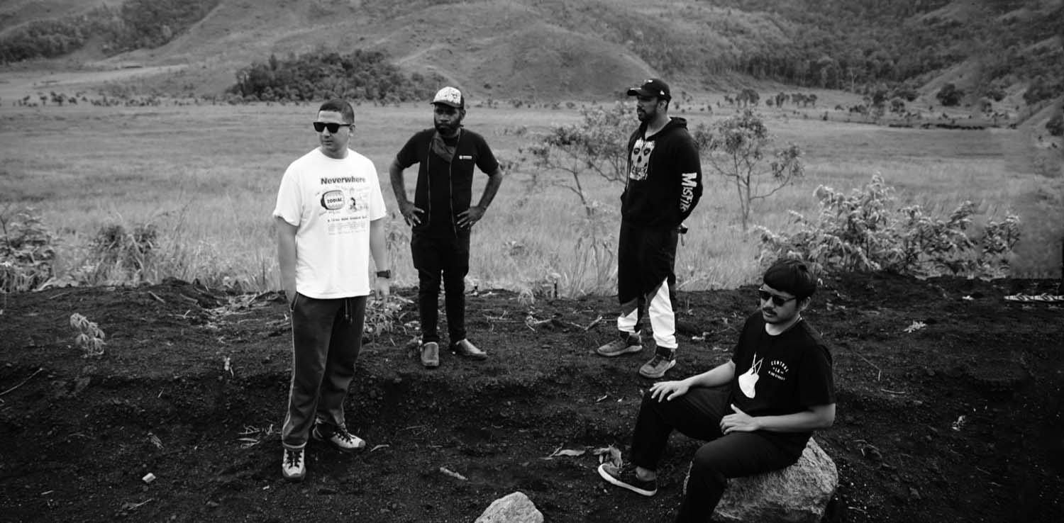 three men standing and one man sitting on a boulder at a field as orpa crew for jendela papua project