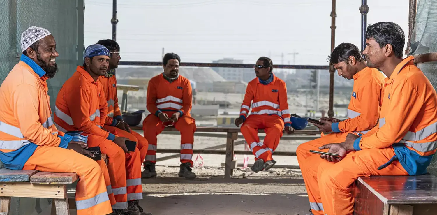 six Qatar world cup workers in orange uniforms sitting together