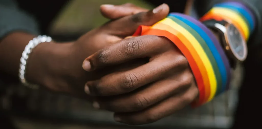 cropped image of intertwined hands, a pride flag is circling the left hand