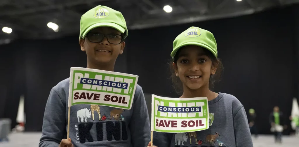 two kids in identical outfits holding a flag that says ‘Save Soil’