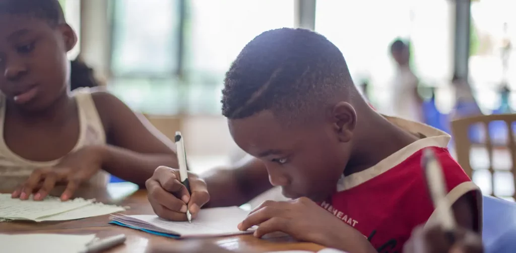 a boy in a red shirt is writing something on a paper