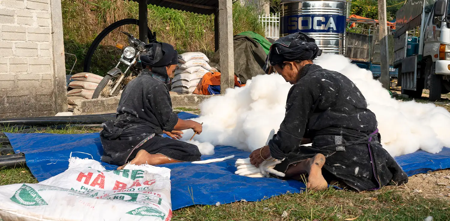 two female workers are working in front of a heap of cotton with their backs facing the camera
