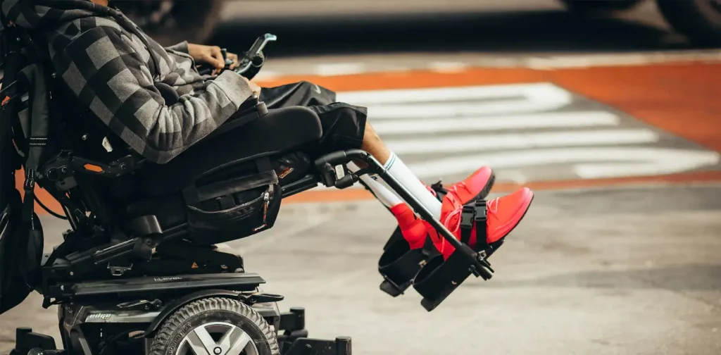 side view of a person wearing red shoes in a motorized wheelchair at a roadside