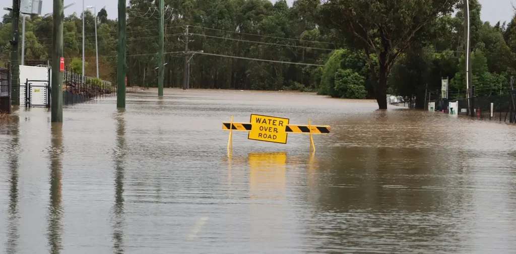 a yellow sign that says “Water Over Road” in the middle of flooded road