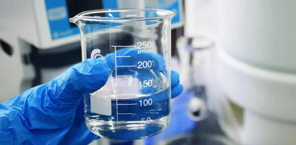a hand clad in blue gloves is holding a clear measuring cup with water in it