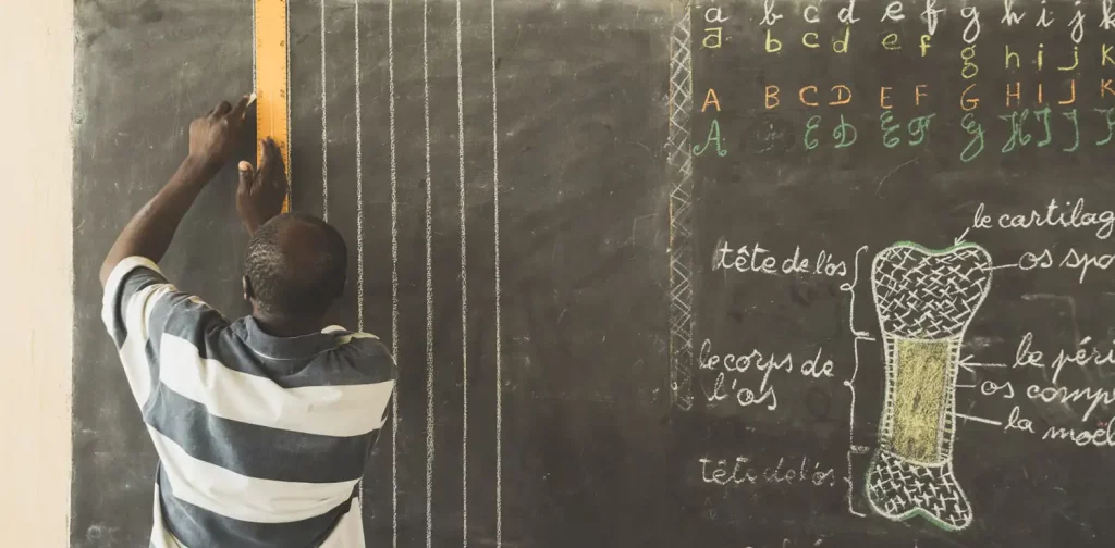 a male teacher drawing on a chalkboard to prepare for his class