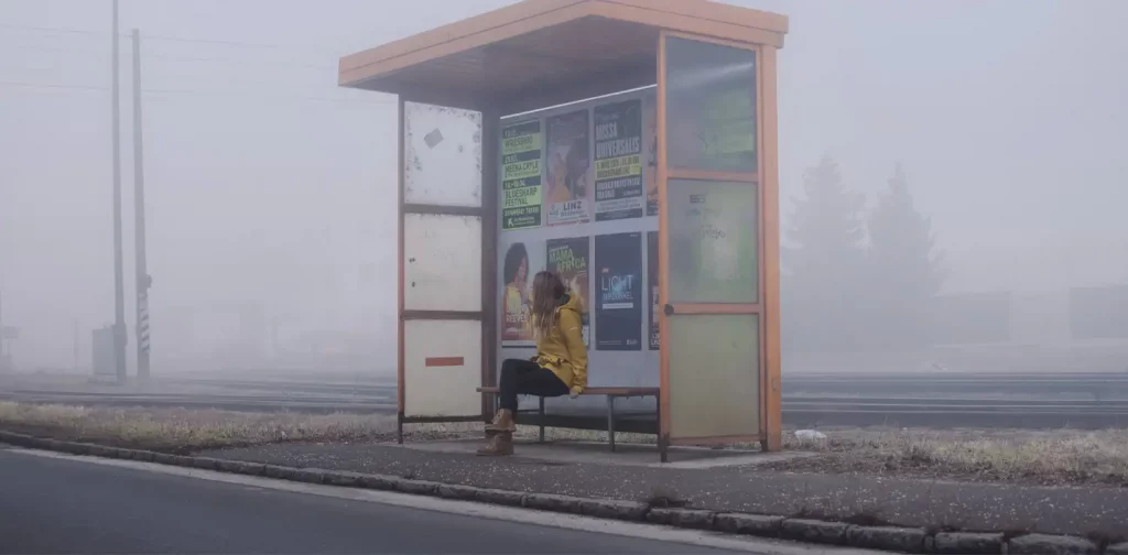 woman sitting at a bus stop with foggy surrounding