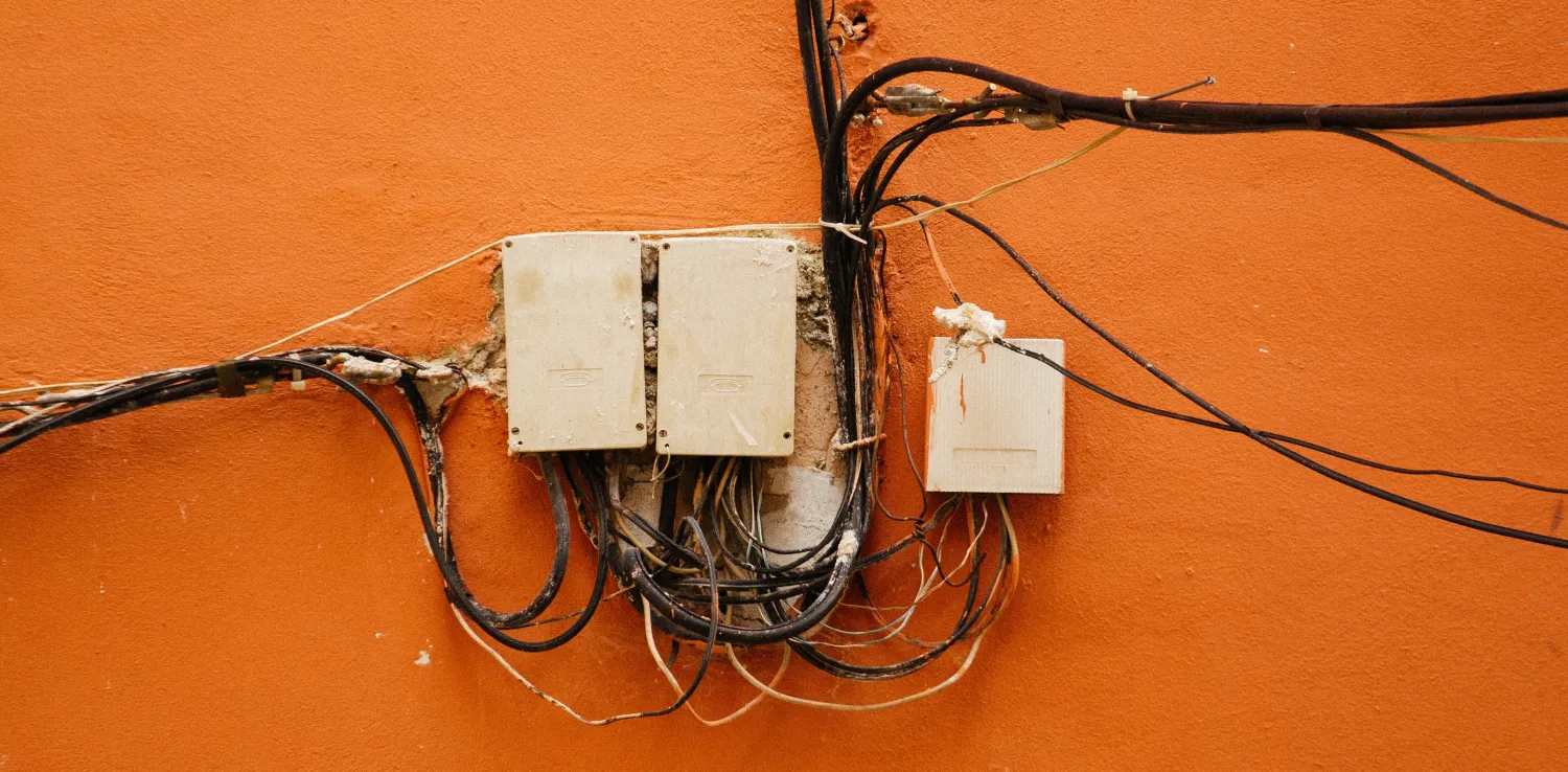 messy wires and three wire boxes attached into an orange wall
