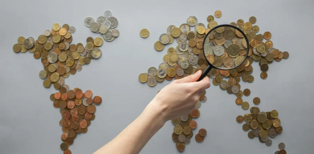 person magnifying view of coins shaped in world map