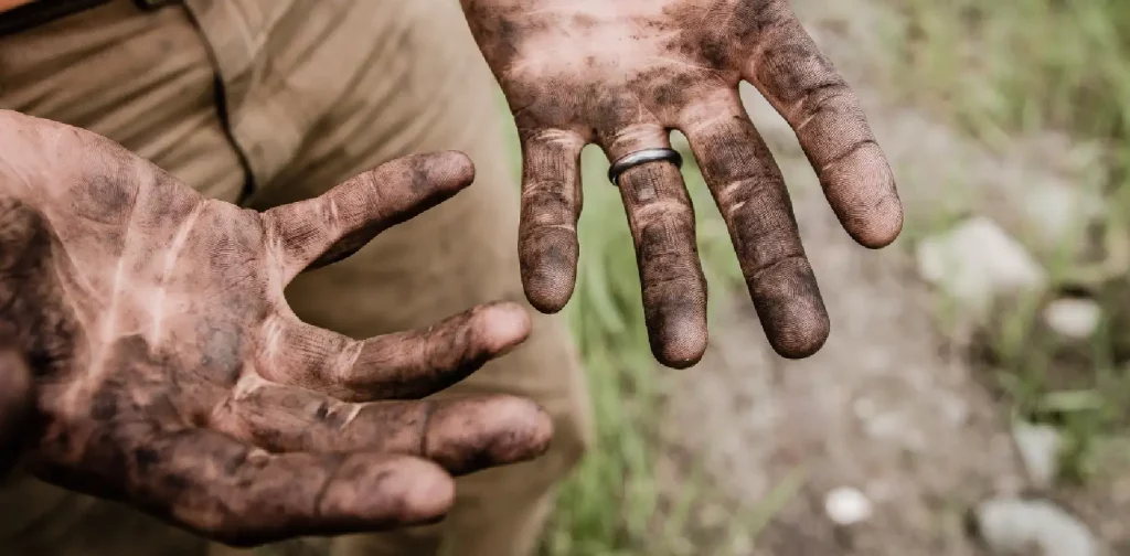 a man with no face showing his two hands that are dirty from soil