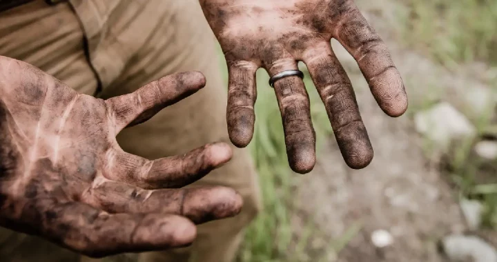 a man with no face showing his two hands that are dirty from soil