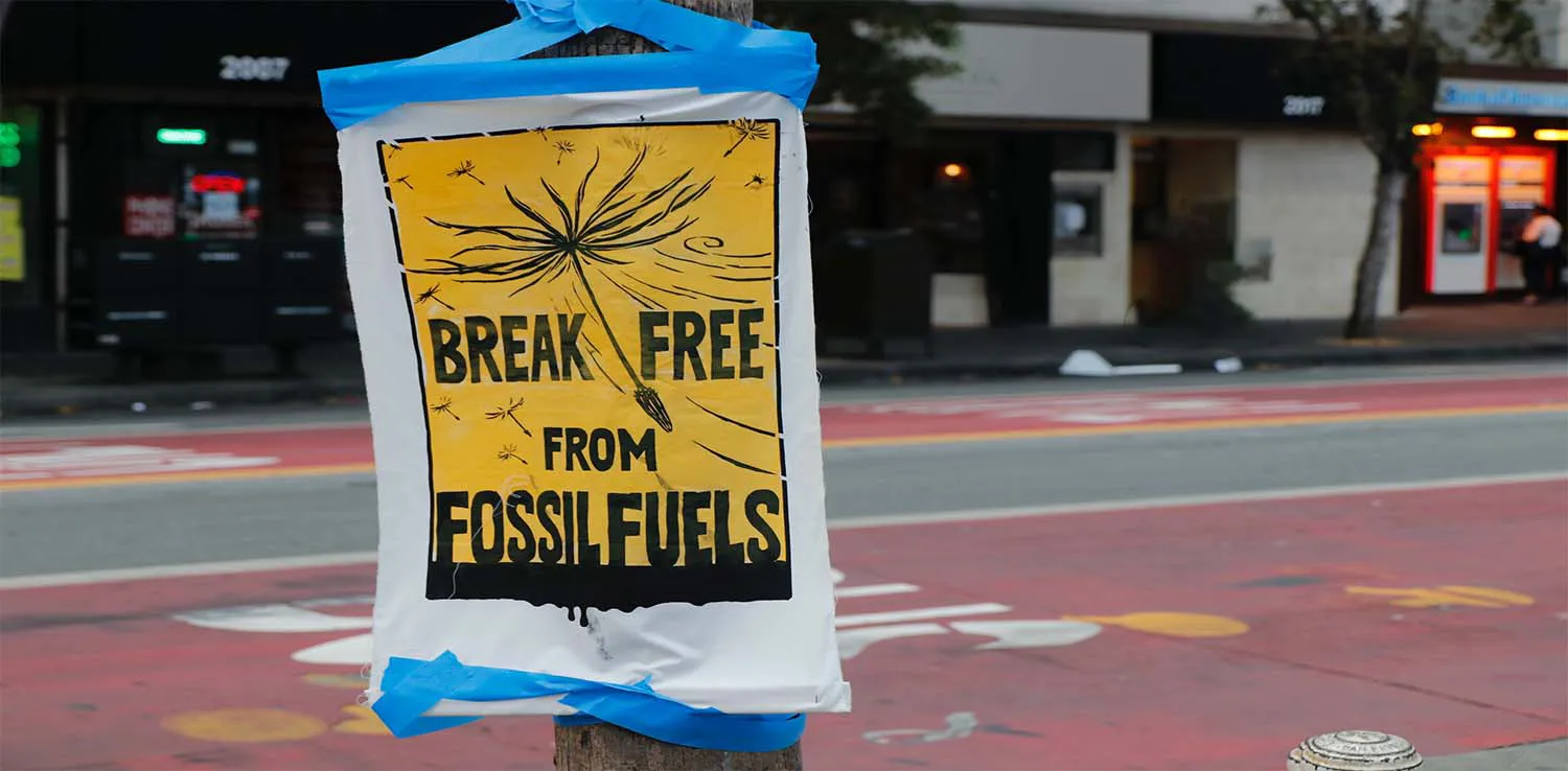 a yellow sign that says “Break Free from Fossil Fuels” plastered on a lamp post.