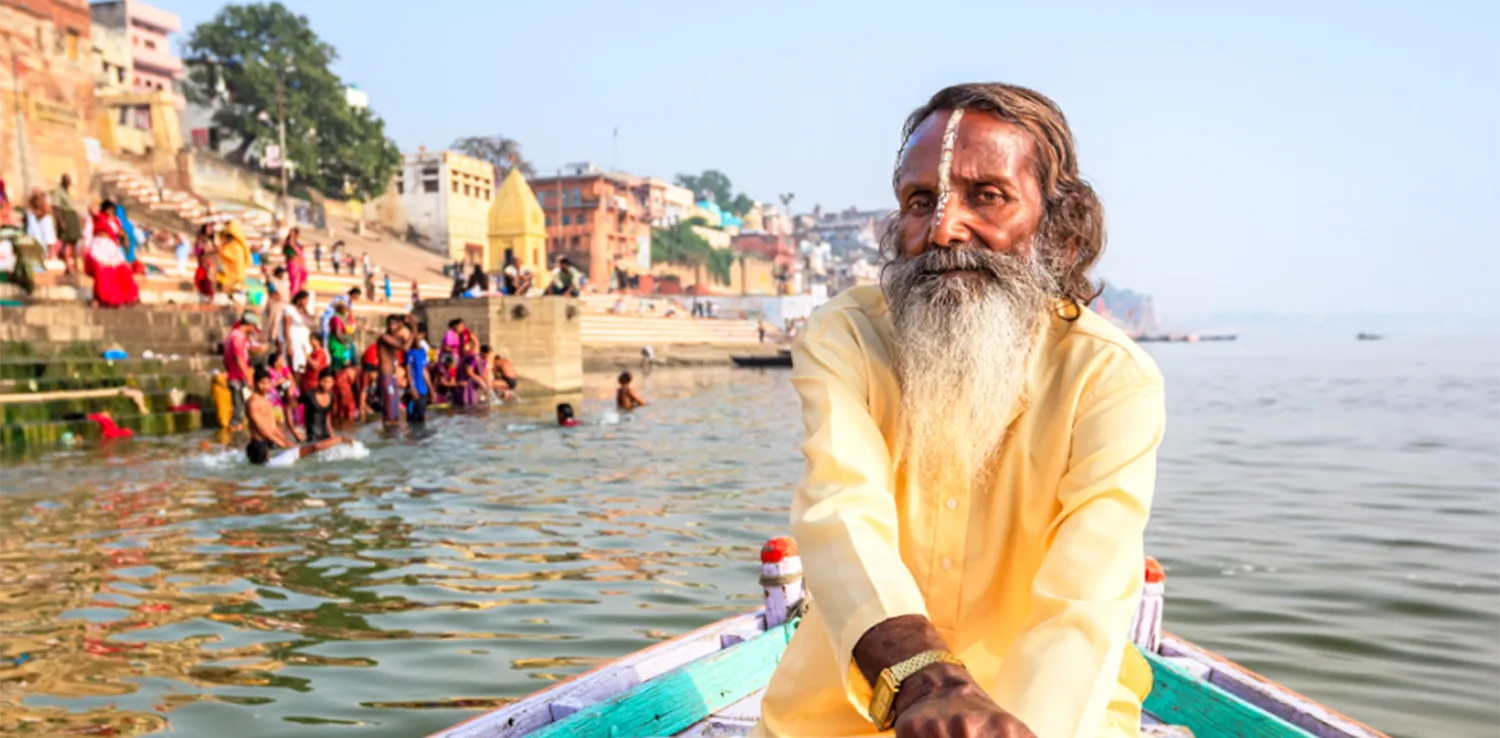 An indian man paddling on a boat on the ganges basin, india, with the riverside houses and people in the background