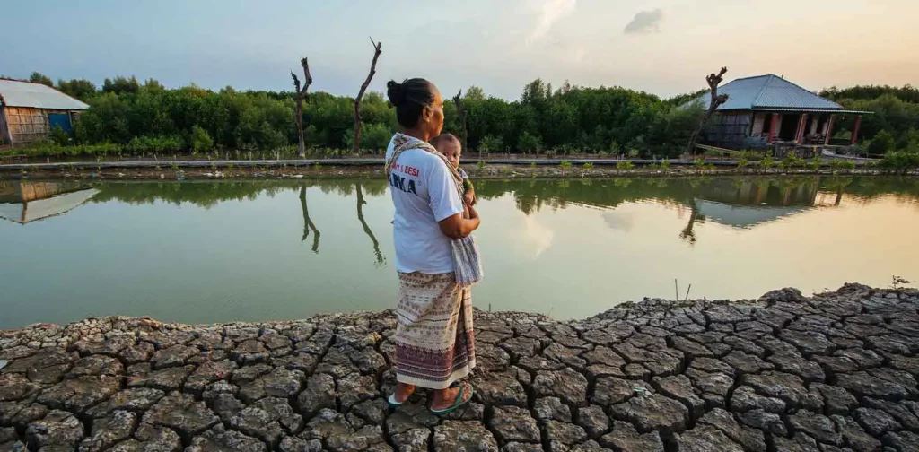 a woman holding a baby at the side of the coast in bedono village, demak, Indonesia