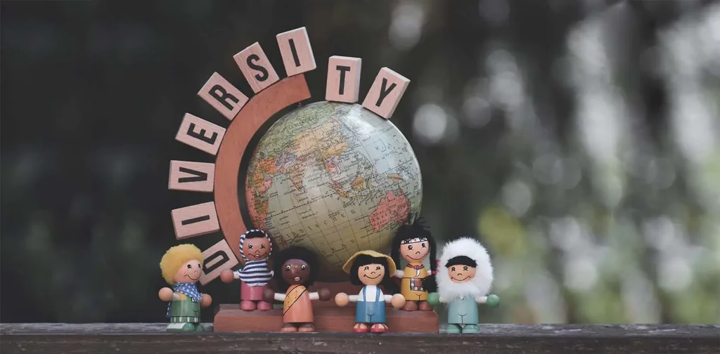 figurines of people with diverse skin colors and clothes lining up in front of mini globes and letter blocks that says ‘DIVERSITY’