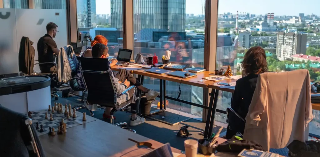 four employees working at a long table near a big window