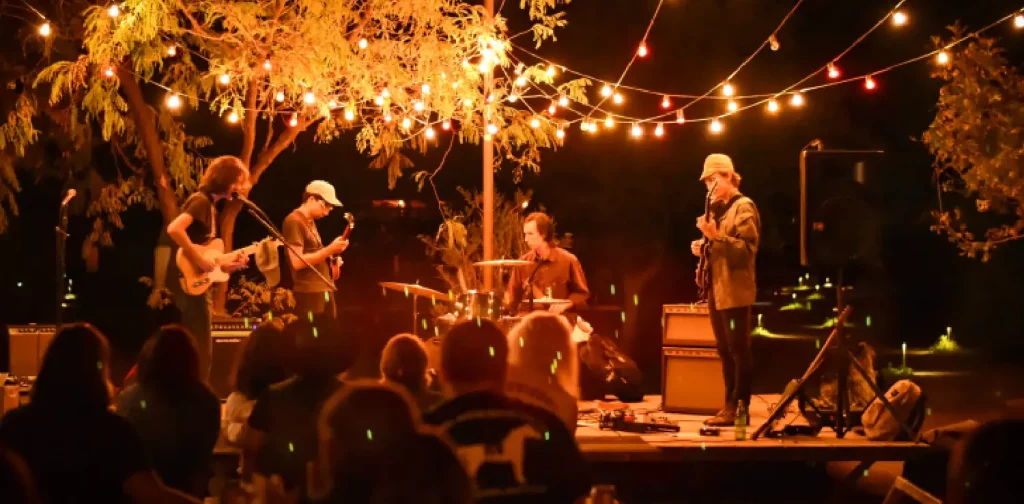 a band with four members are playing in front of audiences under orange-hued lights