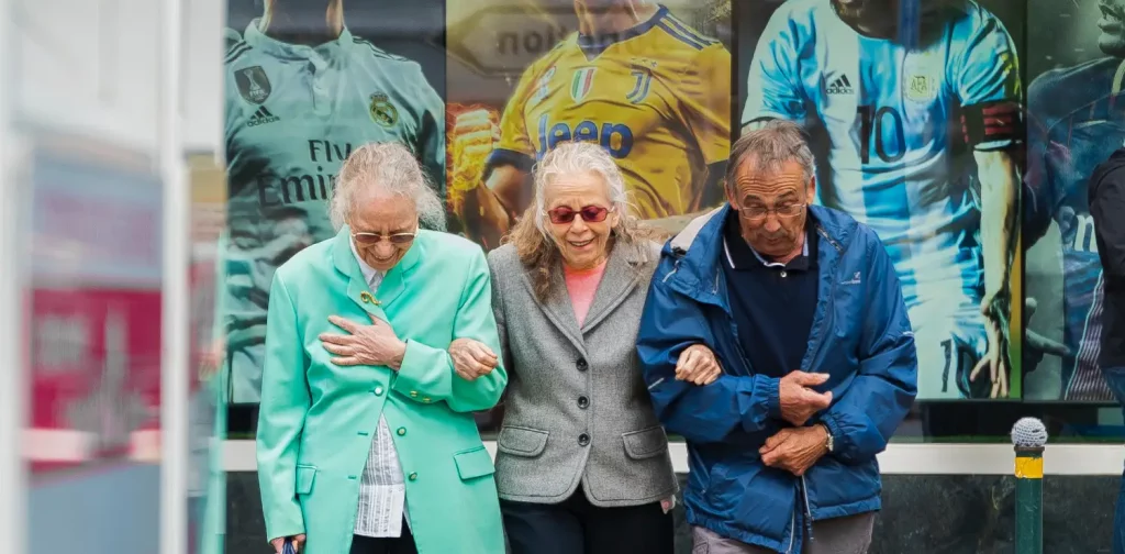 two elderly woman and one elderly man are crossing the street with linked arms