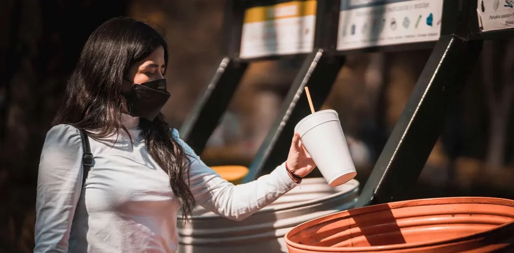 a woman wearing a mask throwing an empty cup to a trash bin