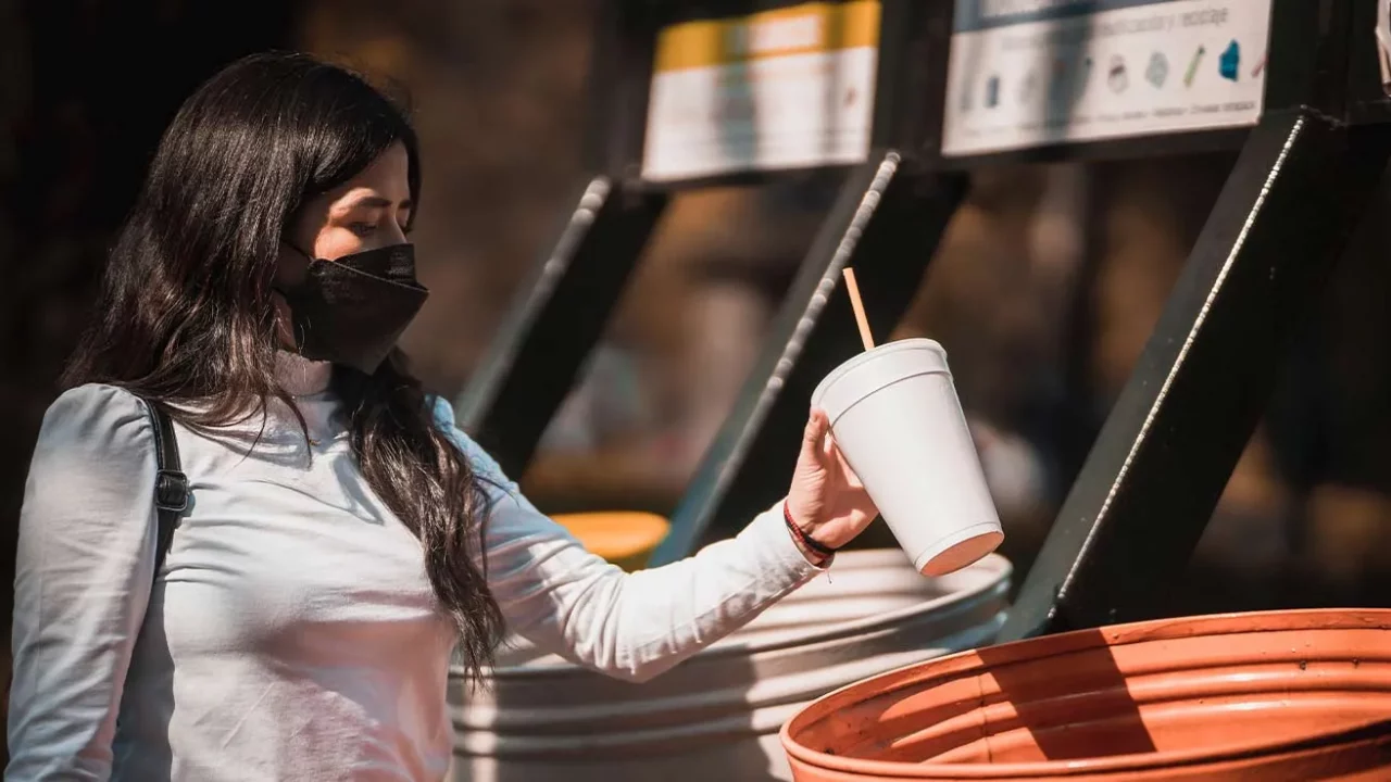 a woman wearing a mask throwing an empty cup to a trash bin
