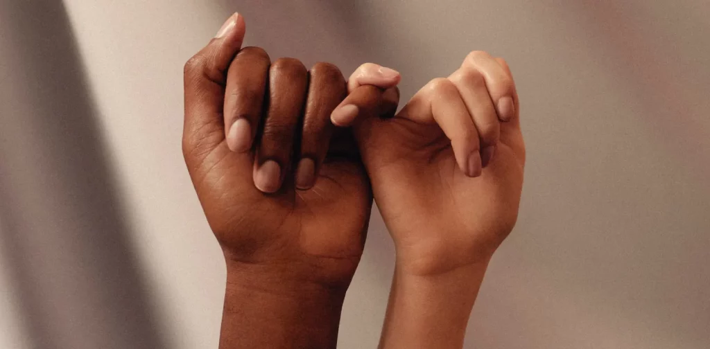 two hands of different race linking pinky fingers