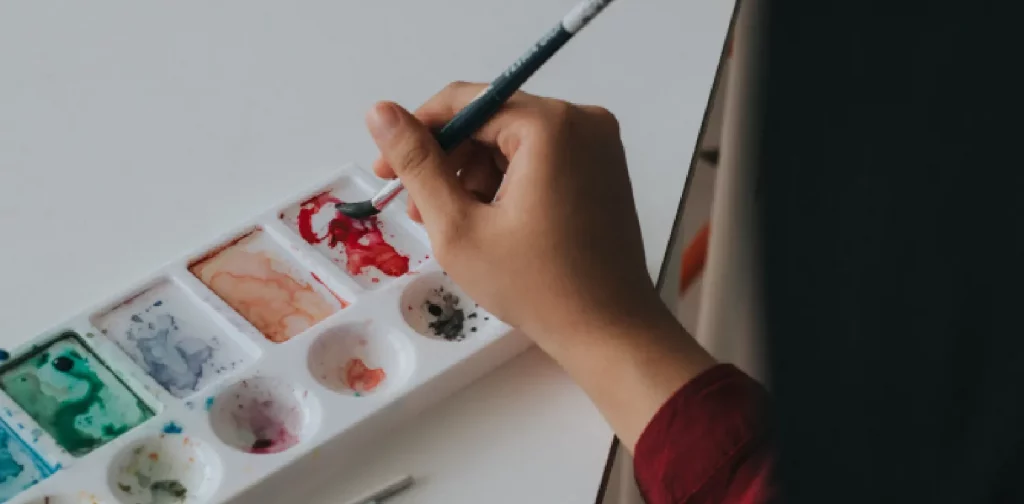 a hand holding a paintbrush above palette