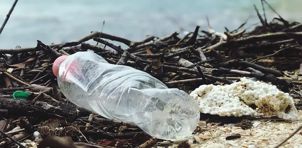 a close up of a plastic bottle trash at the edge of a river