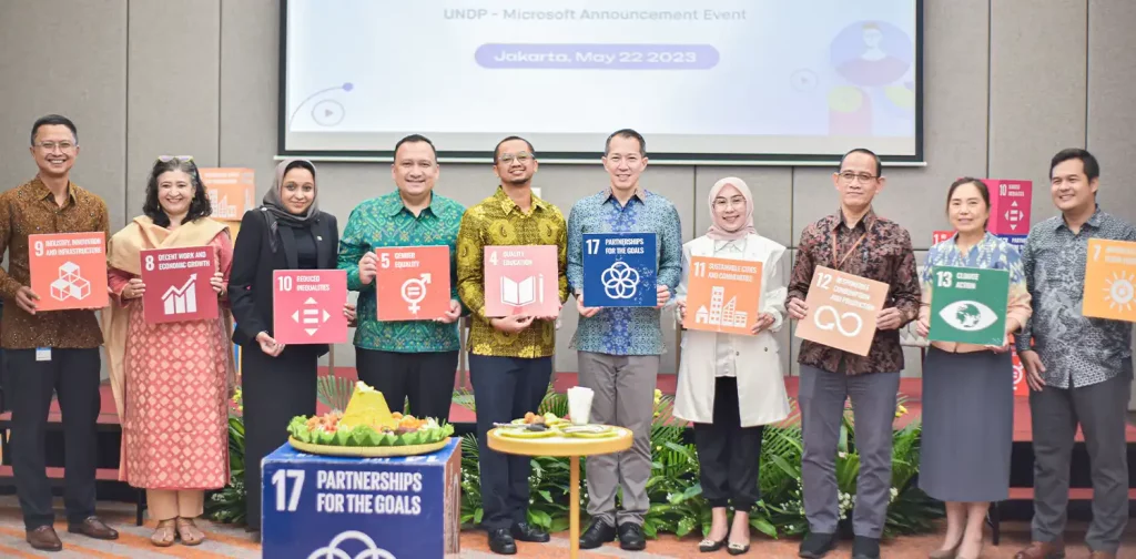 a row of men and women posing in front of a screen holding SDG topic signs at the undp microsoft event in jakarta