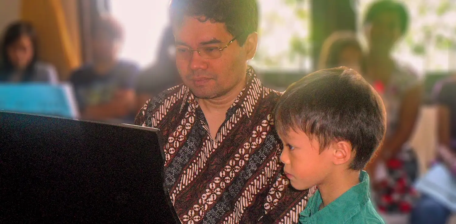 a man, Ananda Sukarlan, is teaching a kid to play piano