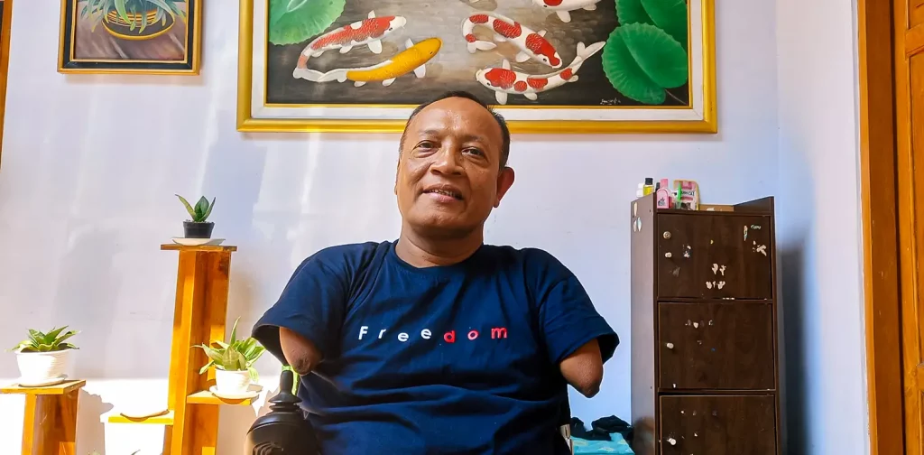 a man with phocomelia in blue t-shirt sitting on a wheelchair in front of a painting