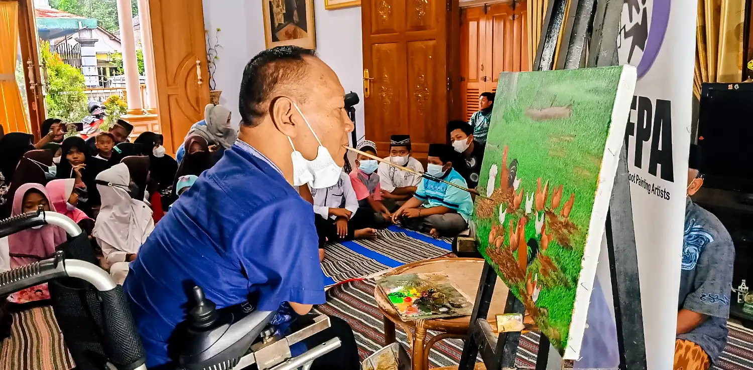 a man painting using his mouth with kids surrounding him 