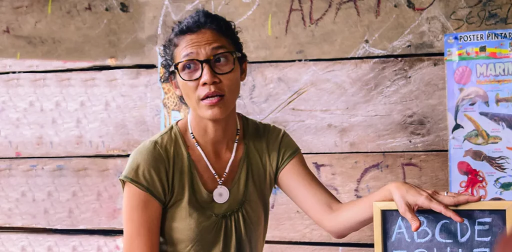 a woman, butet manurung, in glasses holding a blackboard with alphabets on it