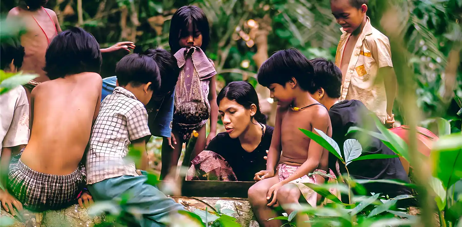 a woman, butet manurung, teaching and surrounded by kids in the middle of the forest