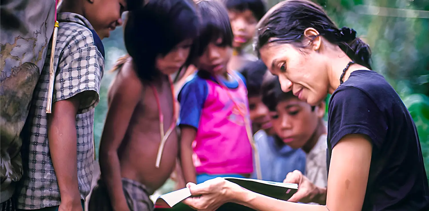 a woman, butet manurung, holding a book and teaching little kids