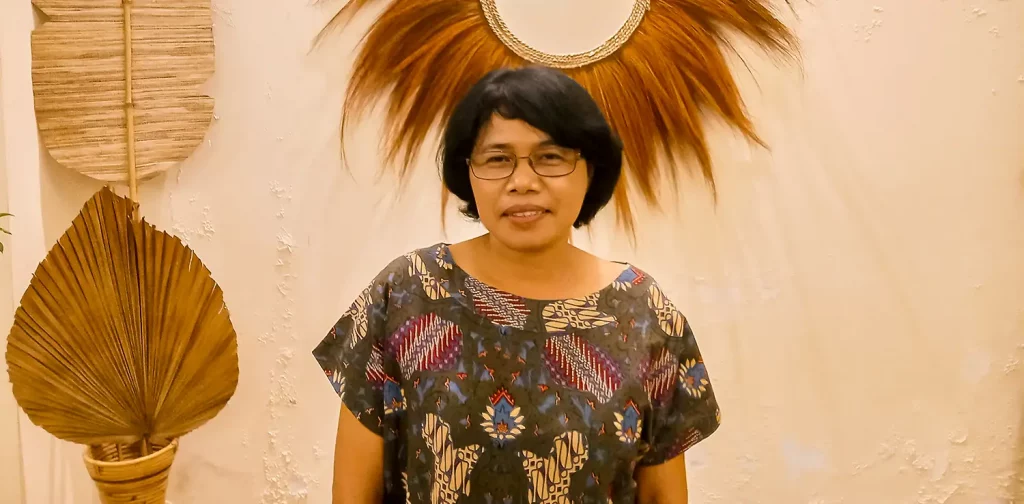 a woman, Indah Darmastuti, sitting in front of a wall with a mirror hanging on it.