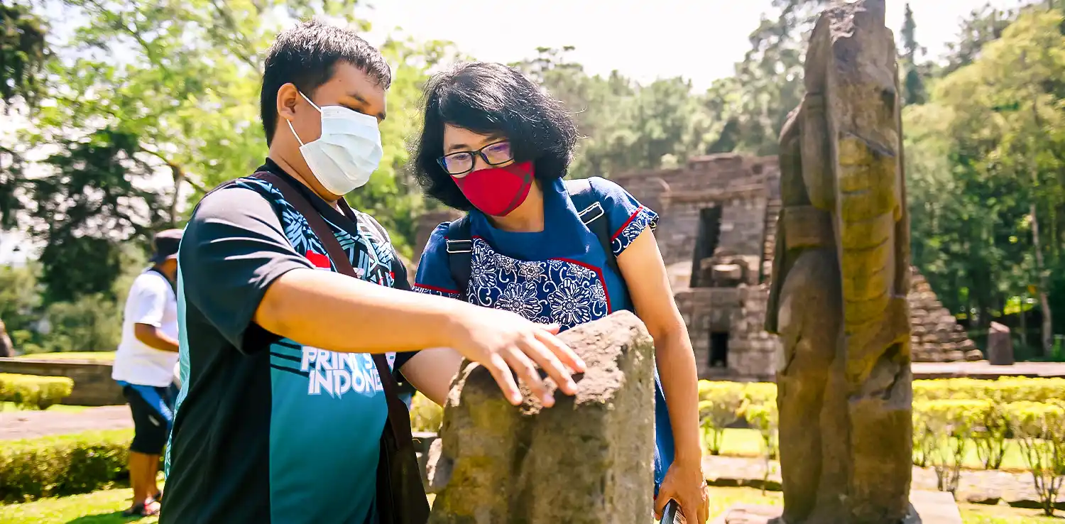 a visually impaired man touching a stone in a temple with a woman guiding him