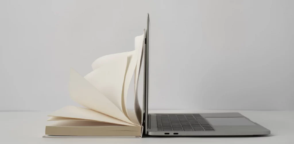 an opened book placed side-to-side with an opened laptop