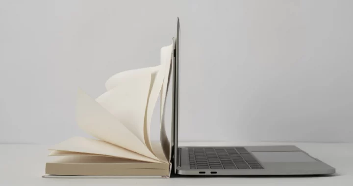 an opened book placed side-to-side with an opened laptop