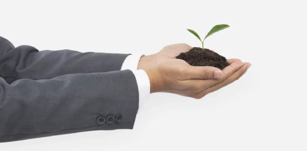 hands clad in suit holding soil with a plant sprouting from it