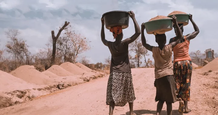 three women carrying basins full of sand while being barefoot