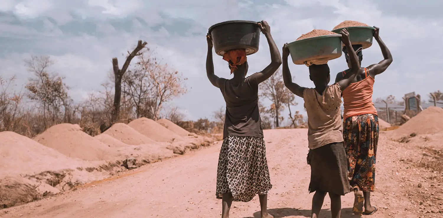 three women carrying basins full of sand while being barefoot