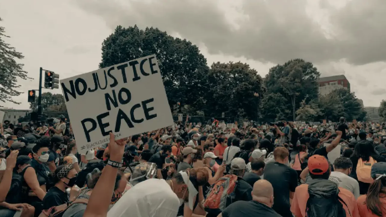 a person holding up a “No Justice No Peace” sign in the middle of a crowd