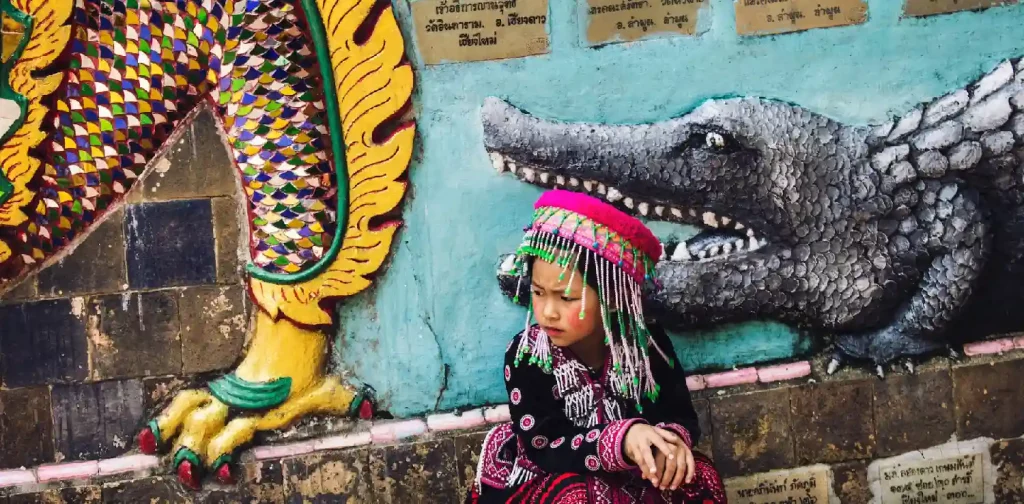 little girl in thai traditional clothing in front of a wall with crocodile mural