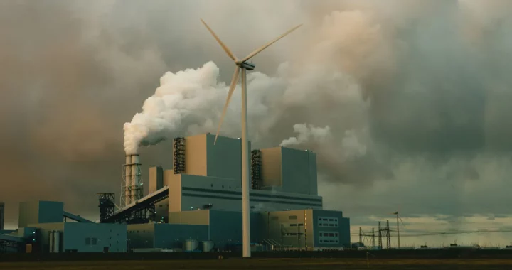 a factory with smoke coming out of its pipes and a windmill placed in front of it