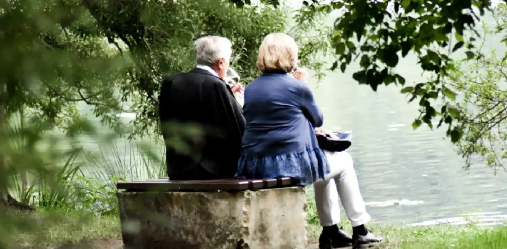 two senior citizens sitting near a lake